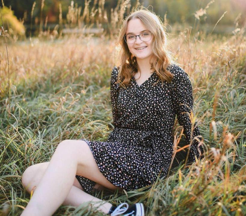 Girl smiling at camera, sitting amongst sunlit wheat grass plants